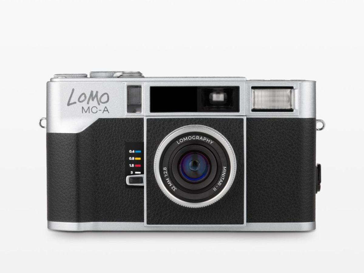 A Lomo MC-A compact film camera with a silver body and black textured front panel, shown from the front against a light gray background.