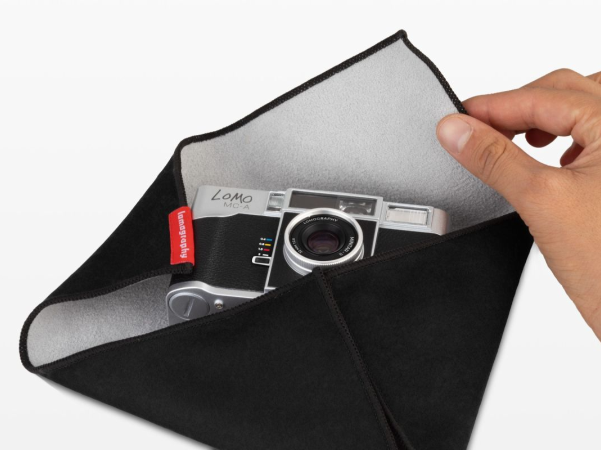 A black camera pouch with a gray interior, shown open with a hand holding the corner. A silver and black Leica camera is partially tucked inside, with a small red brand tag visible.