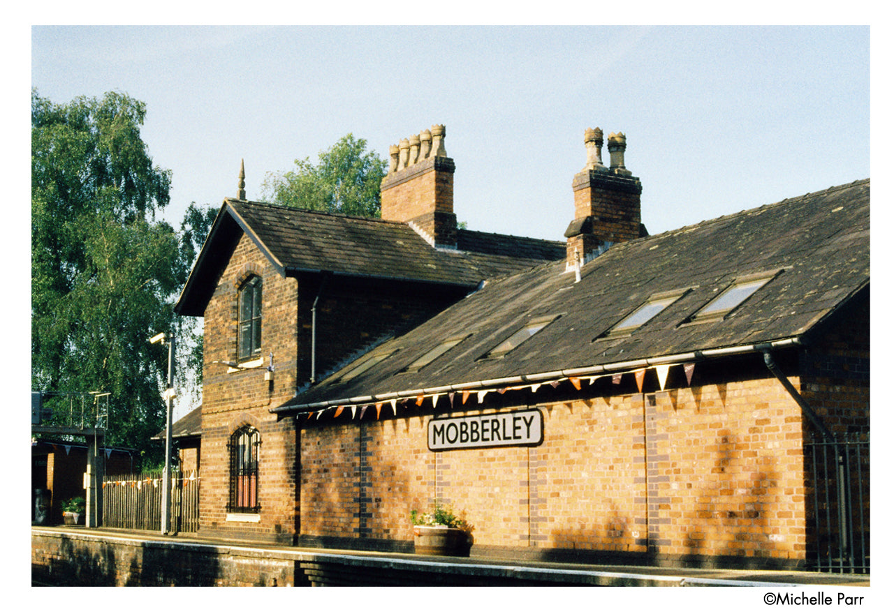 Brick building with 'Mobberley' sign, surrounded by trees and a clear sky - shot on Harman Phoenix II 35mm film