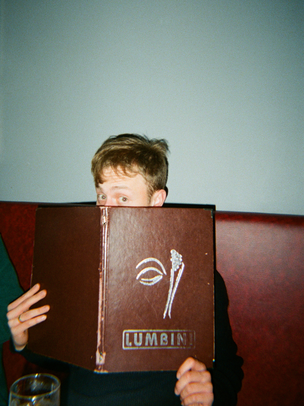 Person holding a menu with 'Lumbin' logo over their face against a plain background - shot on PURE 35 film camera