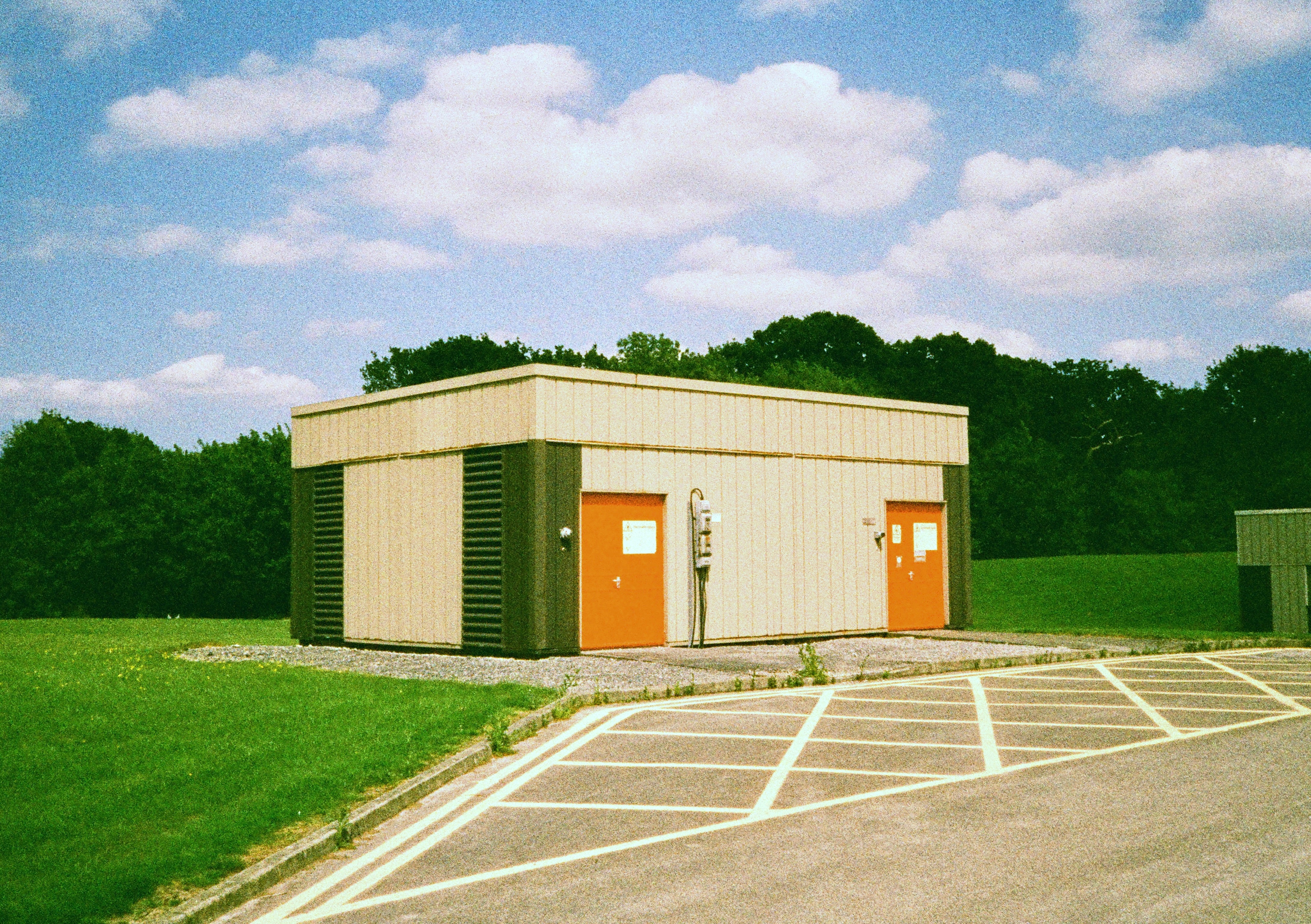 Small building with two doors in a grassy area with trees and a parking lot - shot on Harman Phoenix II 35mm film