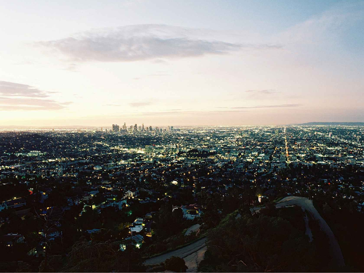 Cityscape at dusk with illuminated buildings and a clear sky.