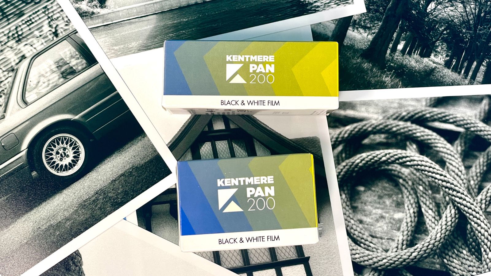 Two boxes of Kentmere Pan 200 black and white film are placed on top of monochrome photographs featuring cars, nature scenes, and coiled rope.