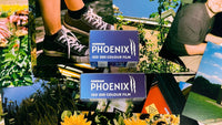 Two boxes of Harman Phoenix ISO 200 colour film (120 and 35mm) placed on a collage of vibrant film photo prints shot on Phoenix II.