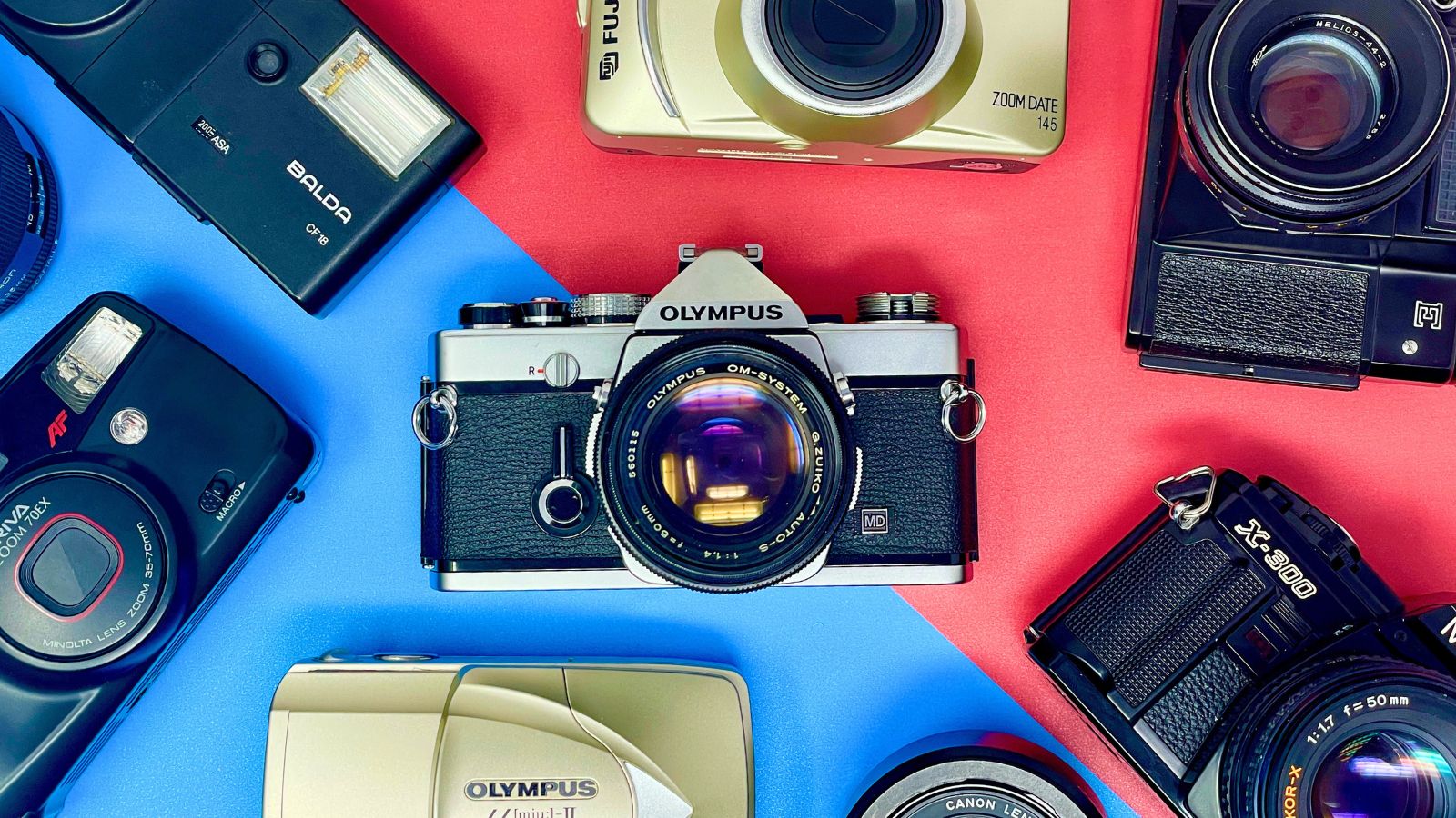 A flat lay of various vintage film cameras arranged on a red and blue split background.