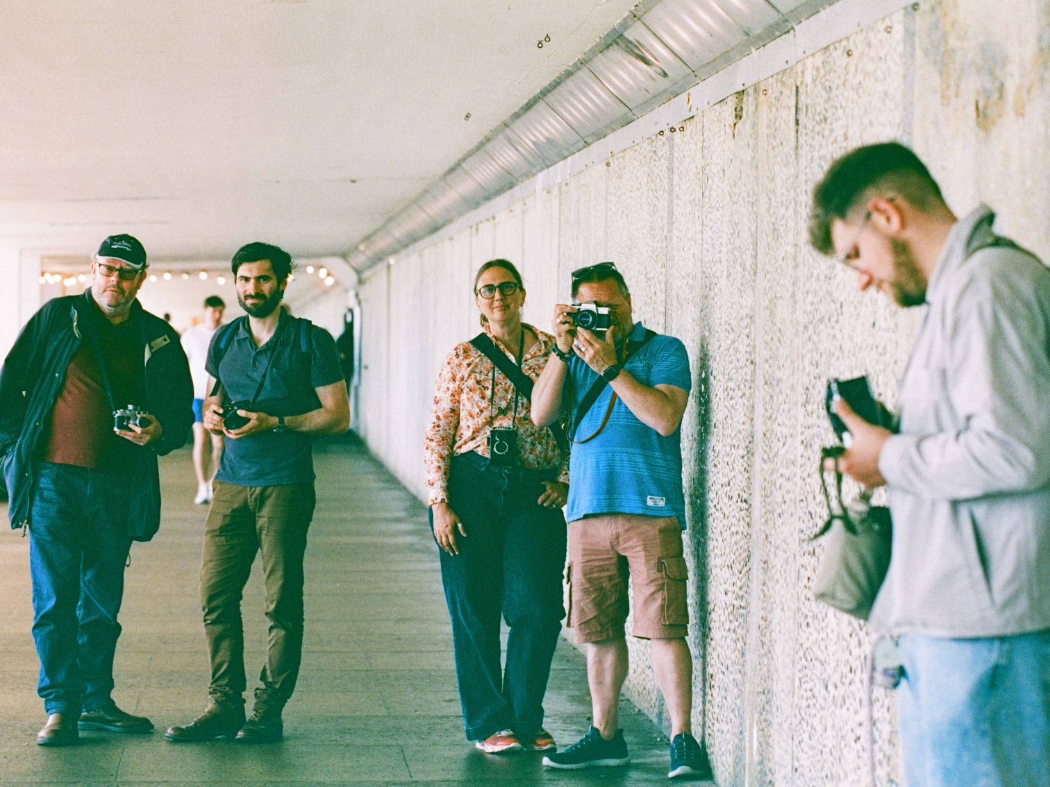 A group of film photographers standing in an underpass, mid-shoot and posing with vintage cameras.