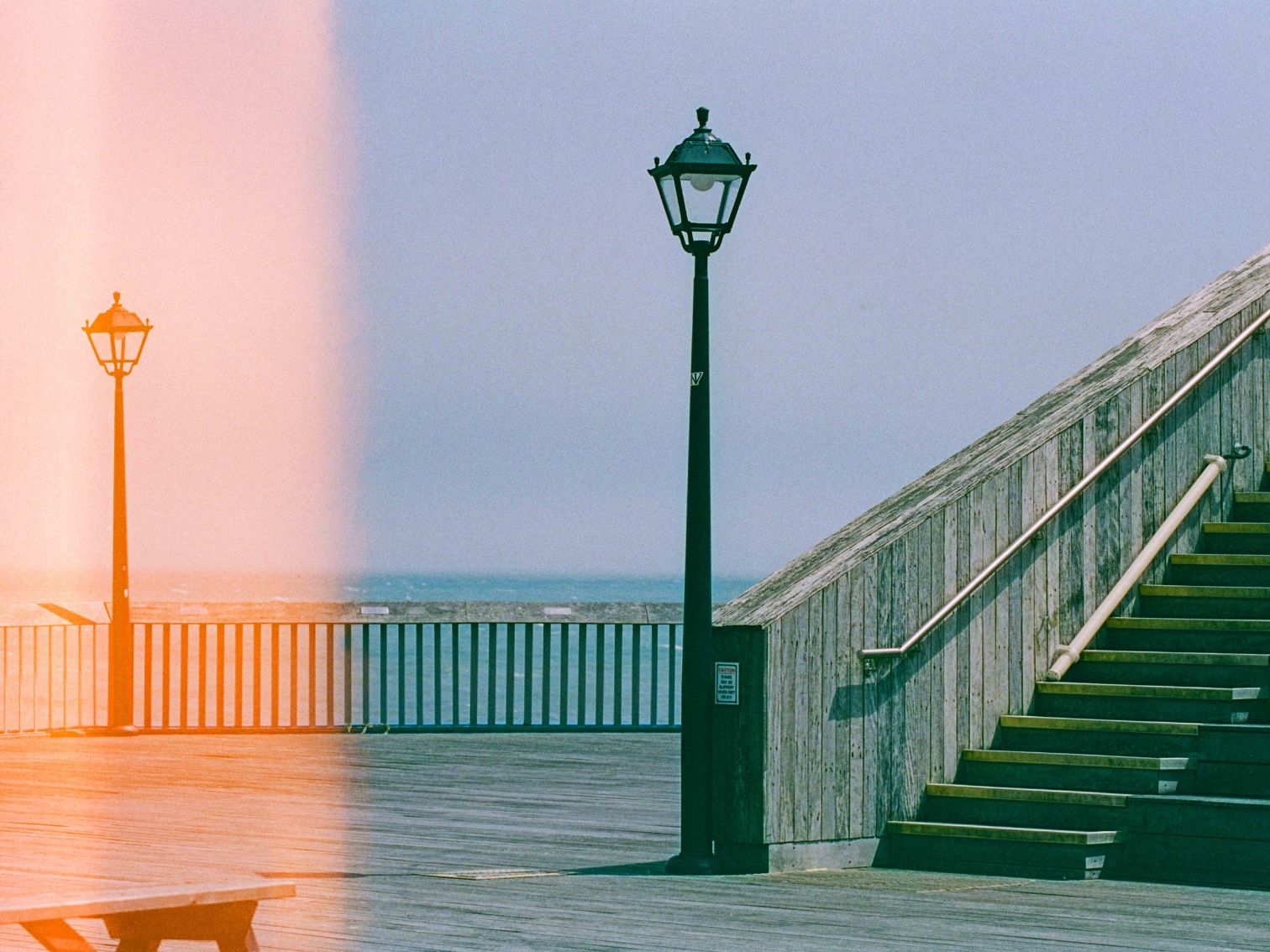 A quiet pier scene with two lampposts and a staircase, partially overexposed with a light leak on the left.