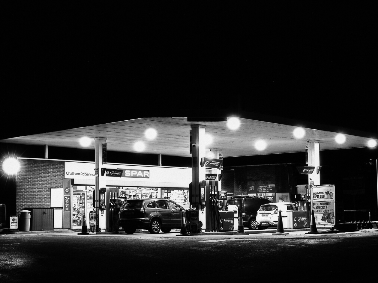 Petrol station at night with illuminated signs and cars.