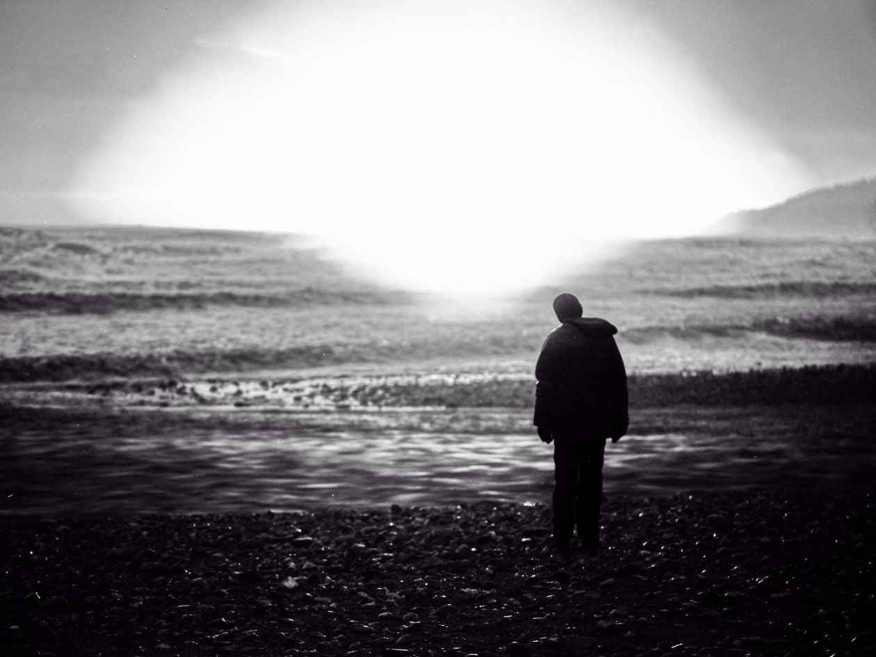 Person standing on a beach looking out at the ocean with a dramatic light effect.