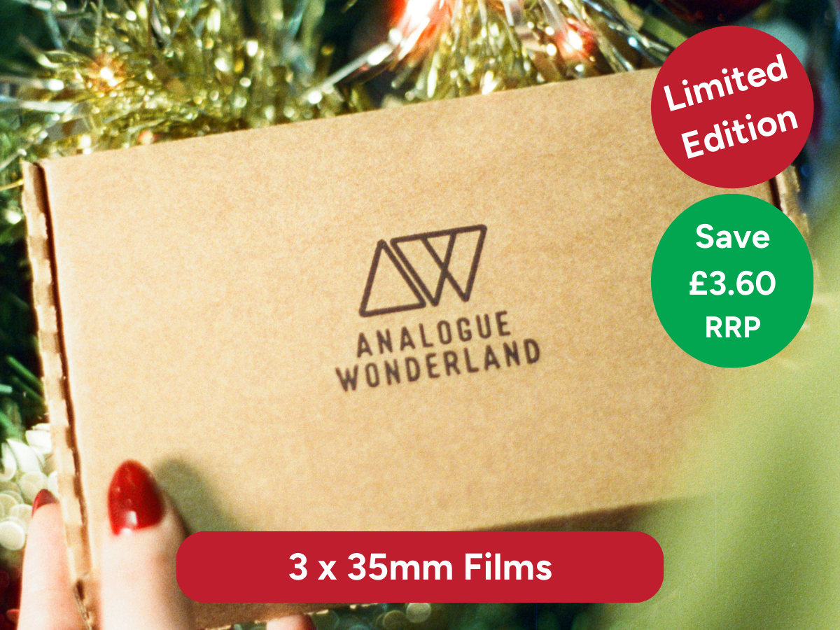 Brown cardboard box with Analogue Wonderland branding, held by a hand with red nail polish against a festive background.