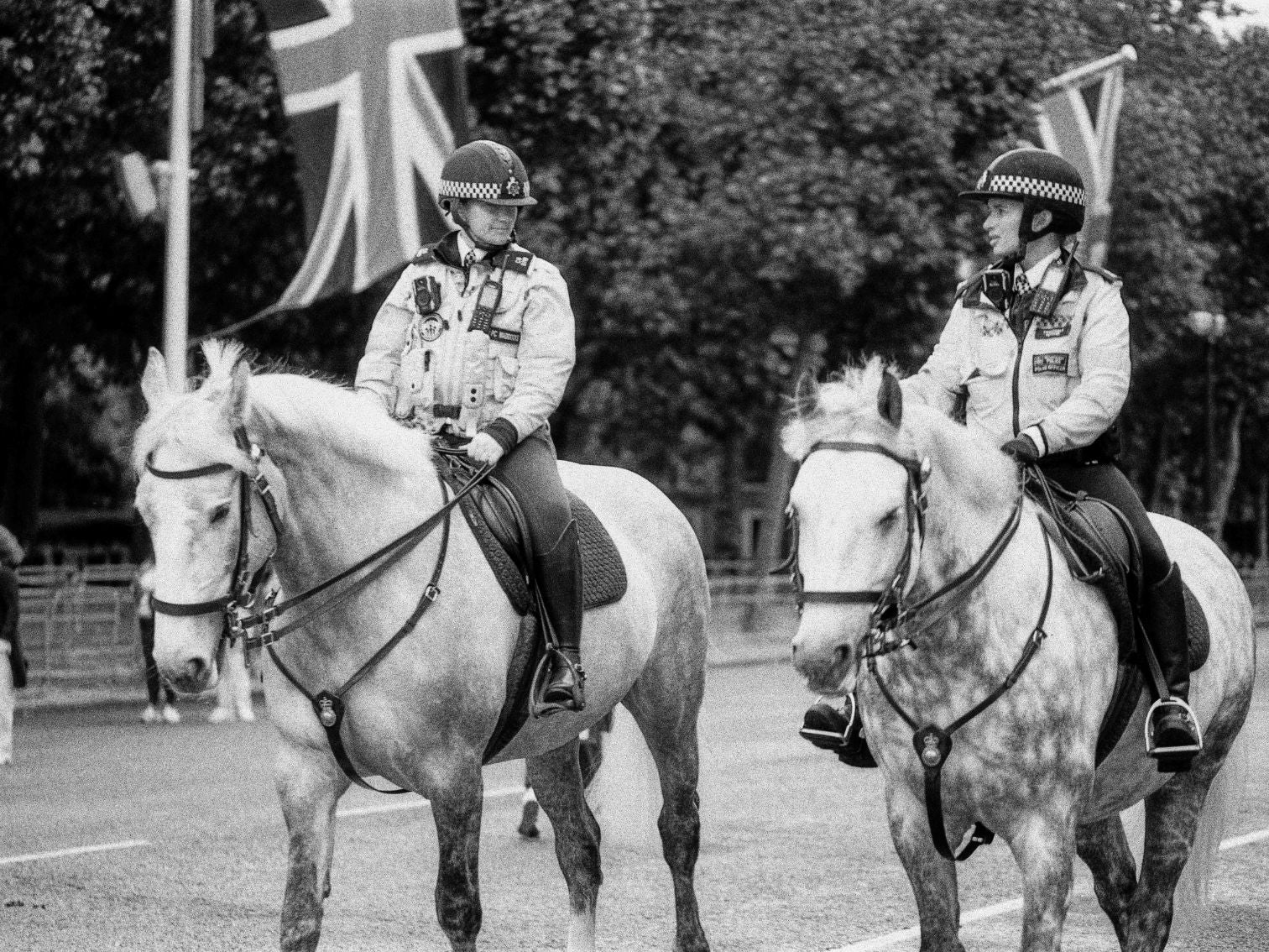 Two mounted police officers in uniform sit astride their horses beneath Union Jack flags.