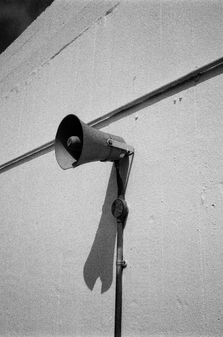 A vintage megaphone mounted on a white concrete wall, casting a bold shadow.