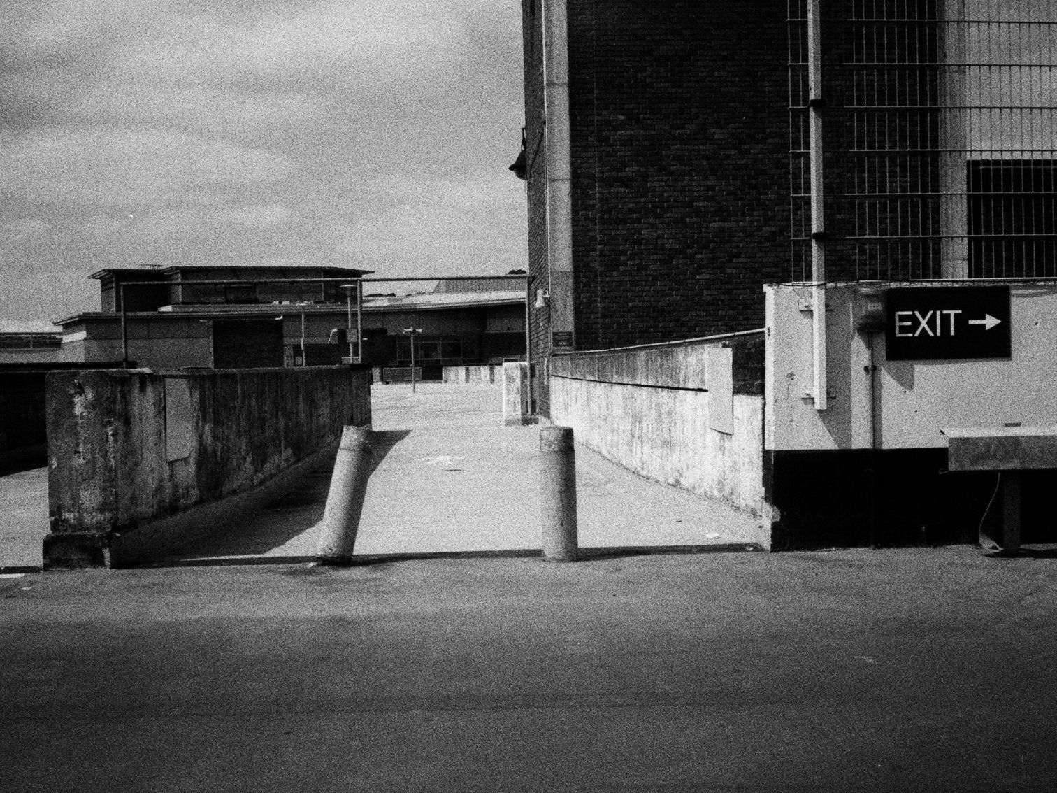 A gritty urban exit ramp between concrete buildings, marked with a bold EXIT sign.