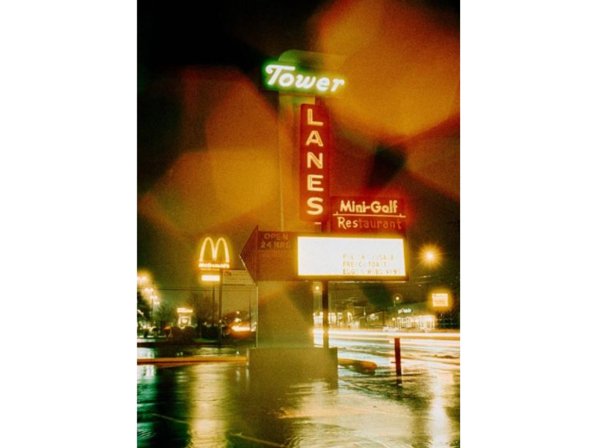 A vertical photographic print of a vintage night street scene featuring the Tower Lanes Mid-Golf Restaurant sign, with a glowing McDonald's arch in the background, captured with warm orange and yellow light leaks and reflections on wet pavement.
