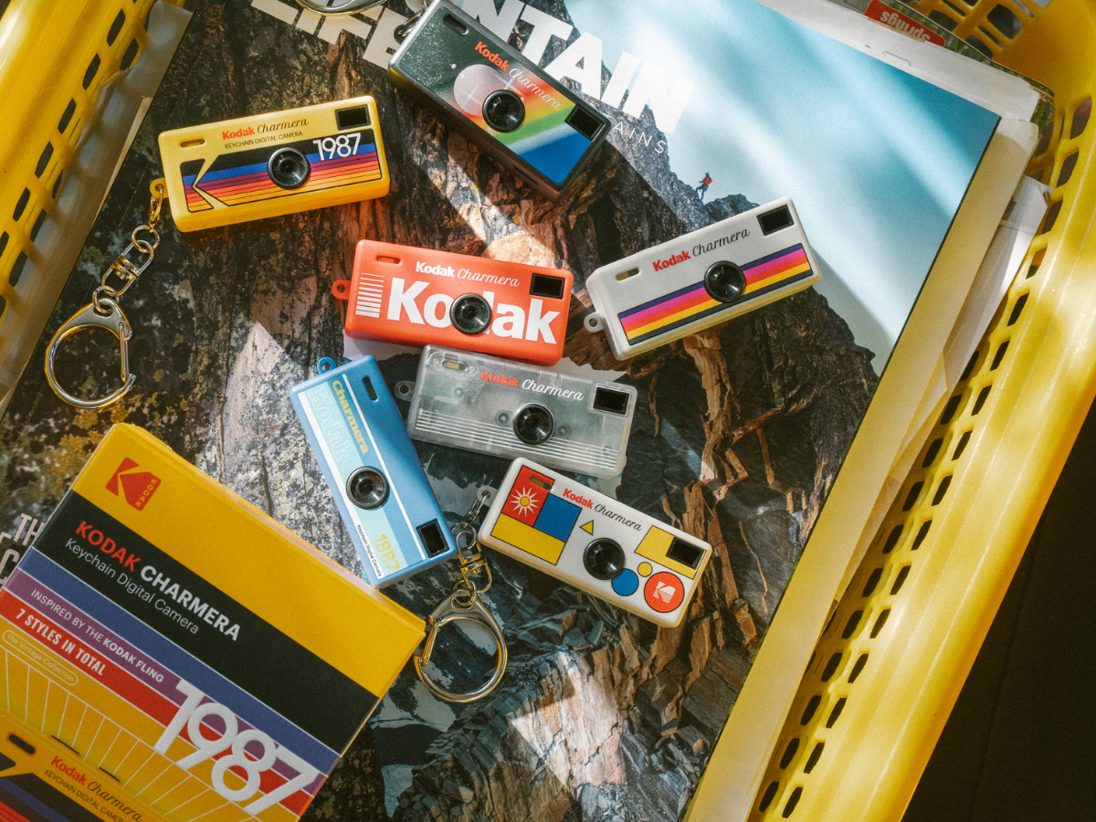 Collection of Kodak Charmera keychains on a textured surface with a magazine in the background.