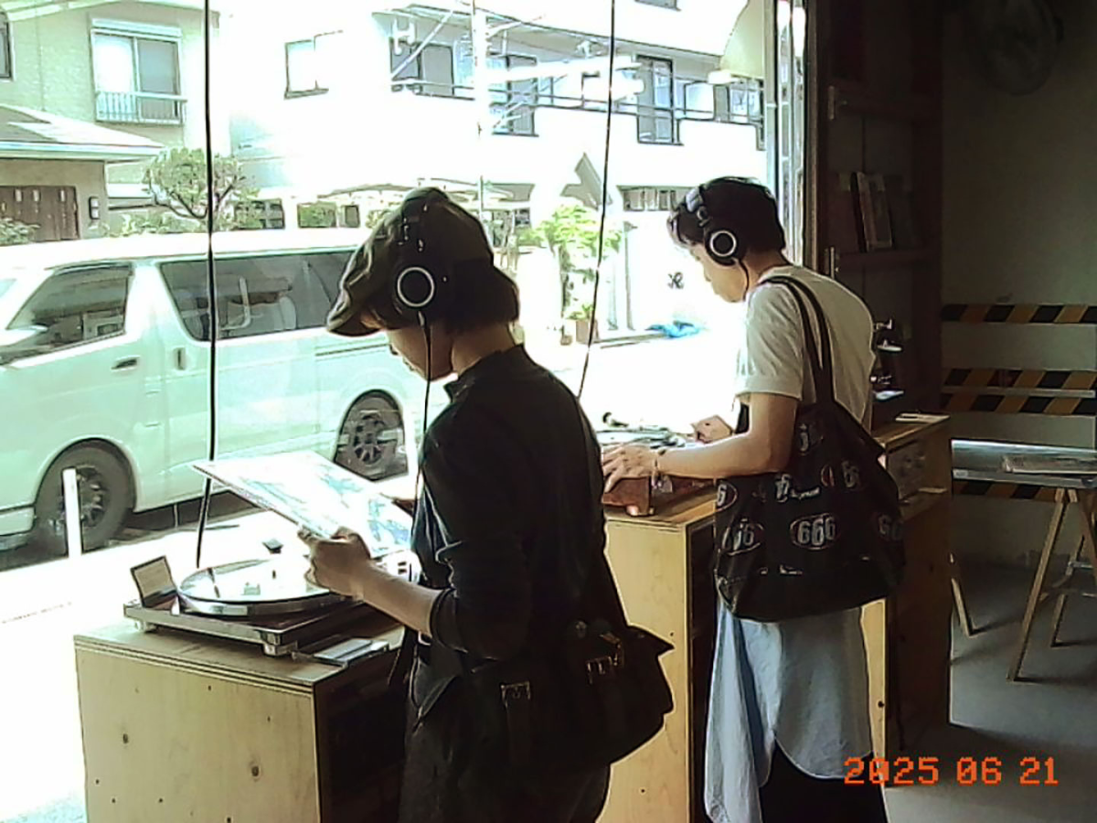 Sample Image | Two people using vinyl record players in a store with a reflection of a car outside.