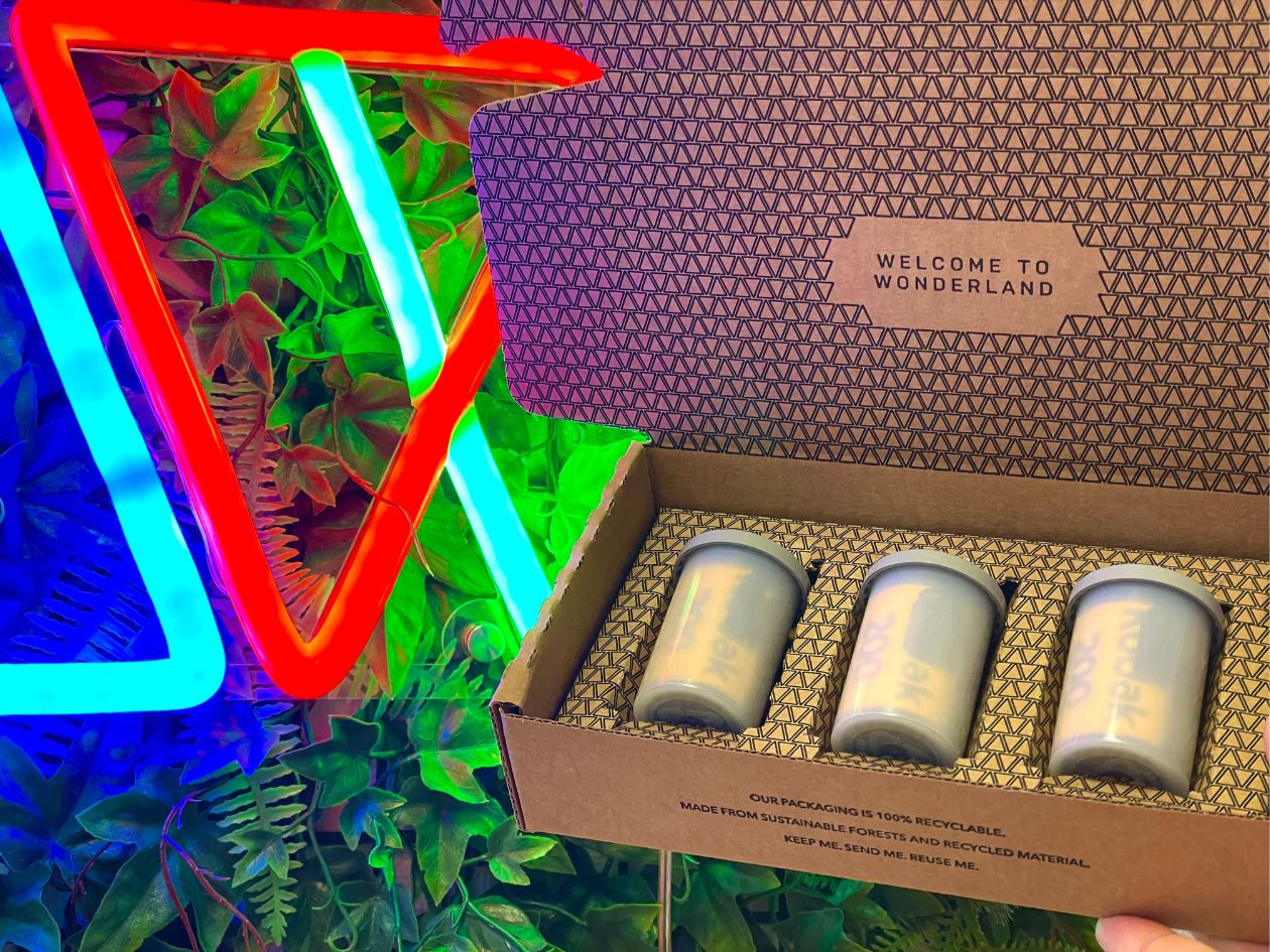 Three rolls of film in plastic pots in a box labeled 'Welcome to Wonderland' with neon lights and plants in the background.