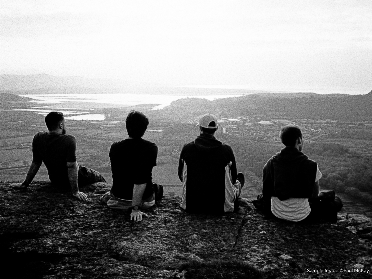 Four people sitting on a rocky outcrop overlooking a landscape.