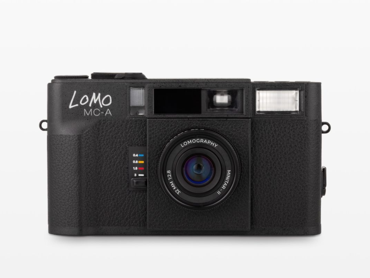 A black LoMO MC-A compact film camera with a textured leather-like finish, shown from the front against a light gray background.