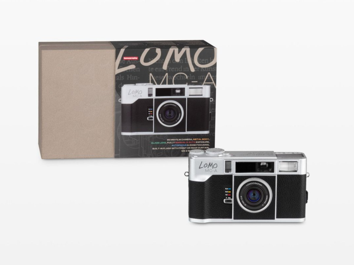 A Lomo MC-1 compact camera with a black and silver body, shown alongside its product packaging box on a light gray background.