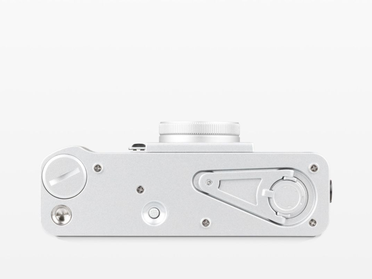 A silver metallic camera body viewed from the top, featuring a textured lens collar, dials, and screws on a clean white background.