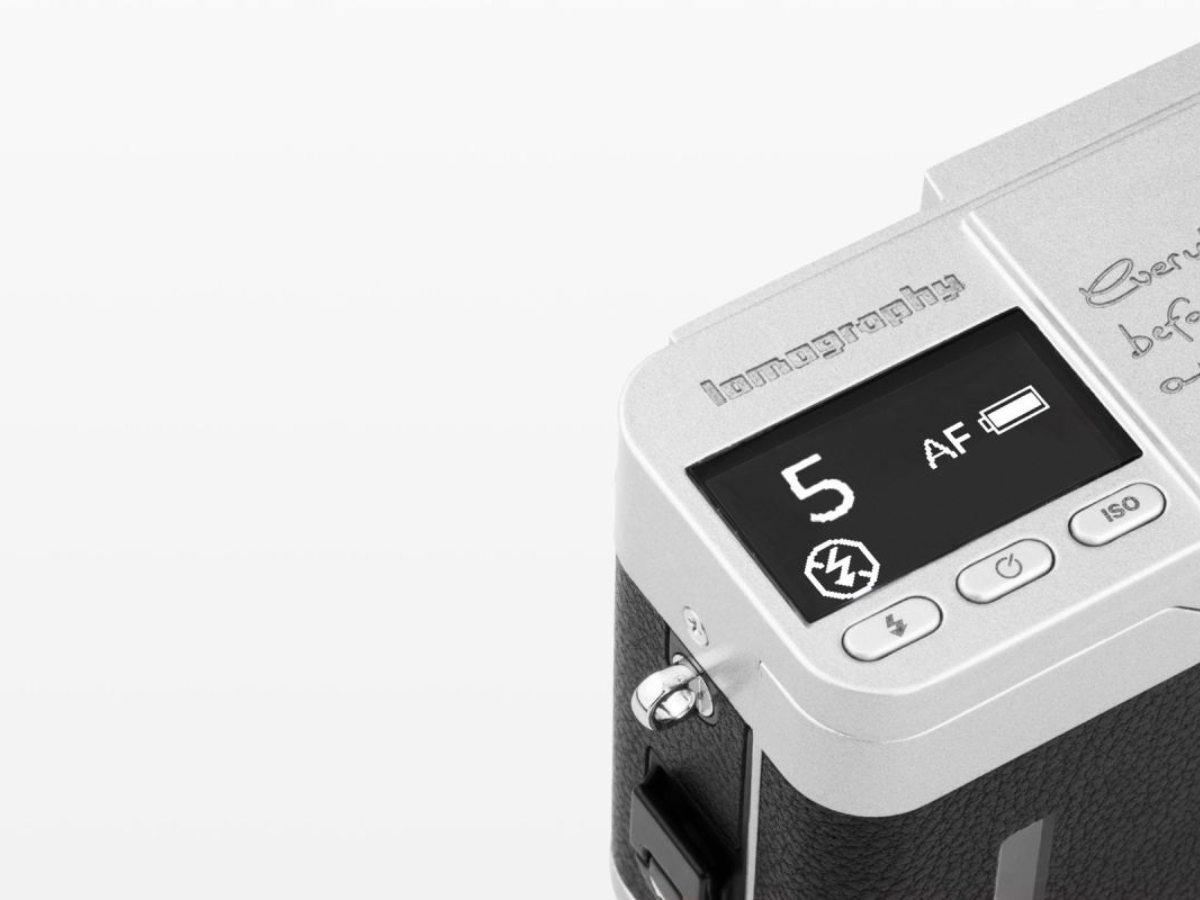 Close-up of a rangefinder-style camera body in silver and black, showing the top control panel with a small display and buttons on a clean white background.