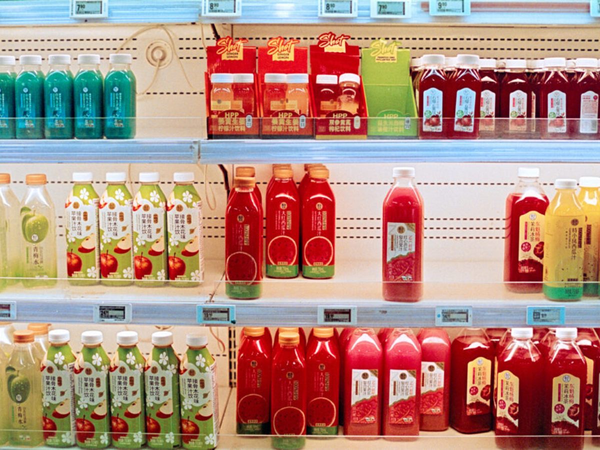 Shelves stocked with bottled and carton juices in a retail store, including red, green, yellow, and white packaged drinks with Chinese labels.