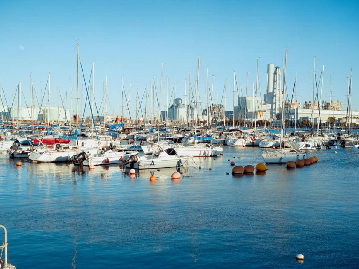 Marina with numerous boats docked, city skyline in the background. (c) Sample Photos by @notmegapixels