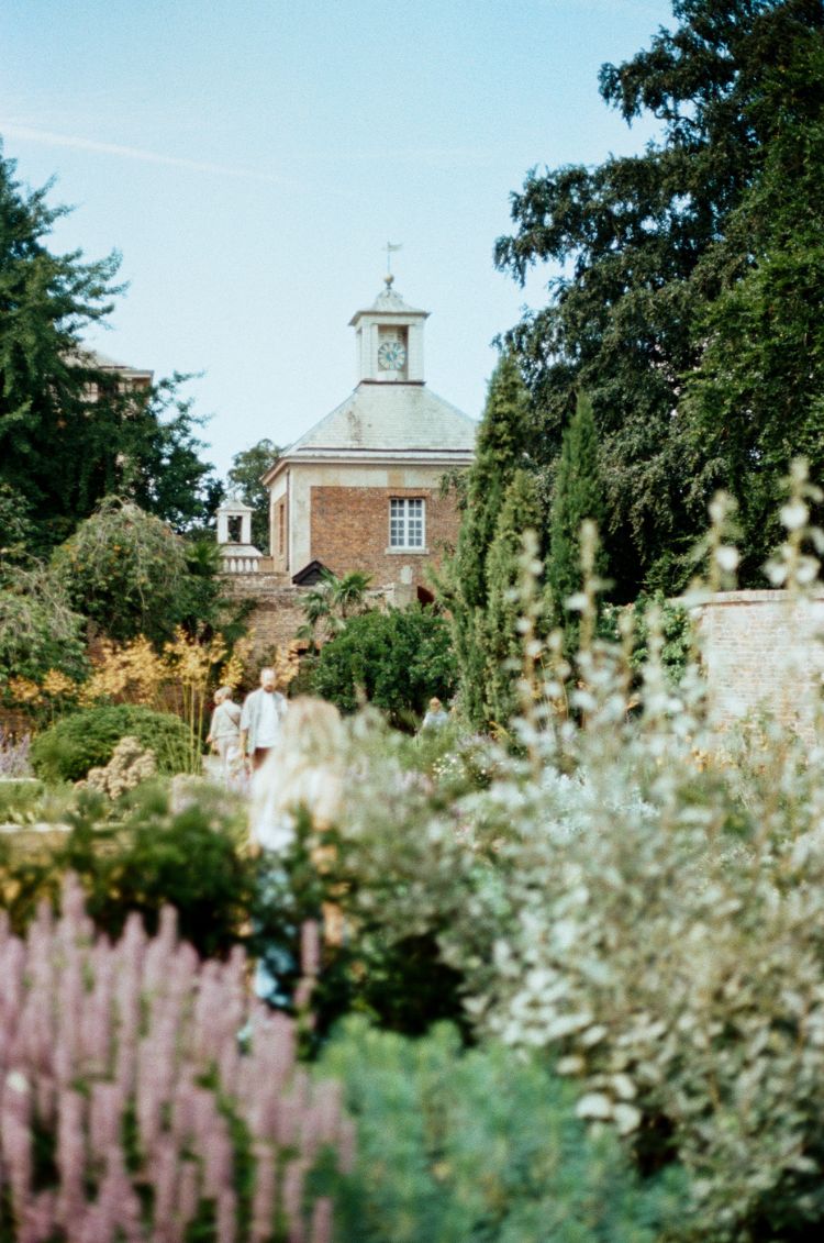 Historic building with a clock tower surrounded by lush greenery and flowers. Taken on Mr Negative Secret Sauce 35mm Film by Gary Smith.