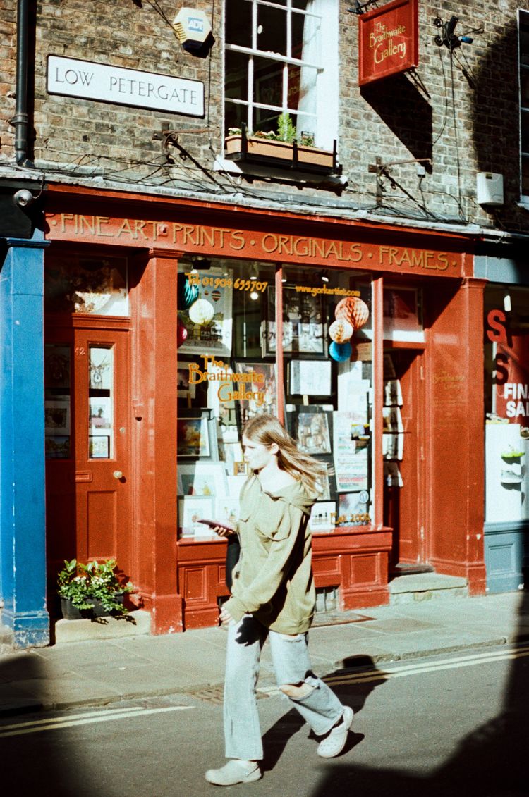 Woman walking past a store with a red facade on a street in London. Taken on Mr Negative Secret Sauce 35mm Film by Gary Smith.