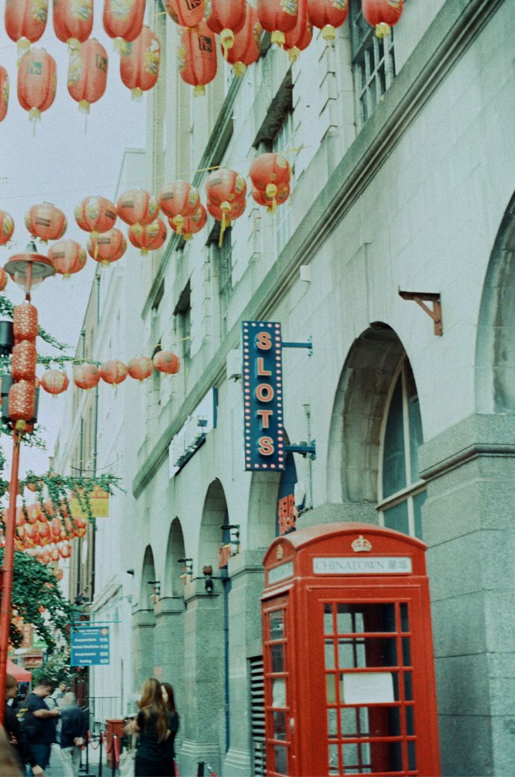Traditional Chinese lanterns hanging above a building with a red telephone booth in an urban setting. Taken on Mr Negative Secret Sauce 35mm Film by Azucena Morales.