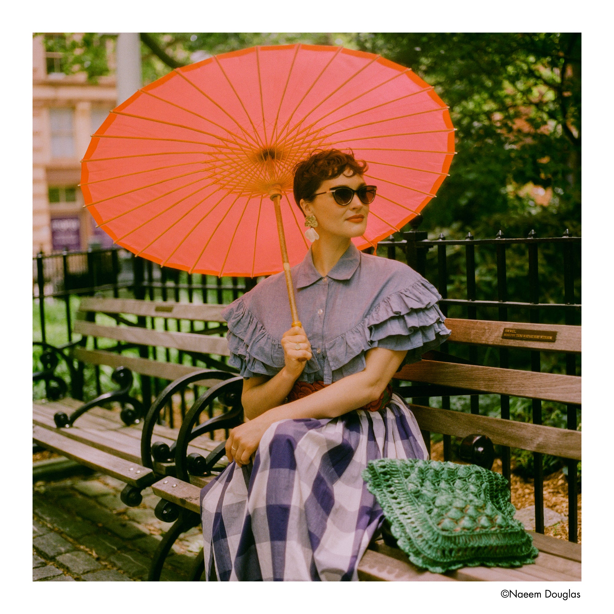 Woman sitting on a bench holding an orange parasol in an urban park setting- shot on Harman Phoenix II 120 film