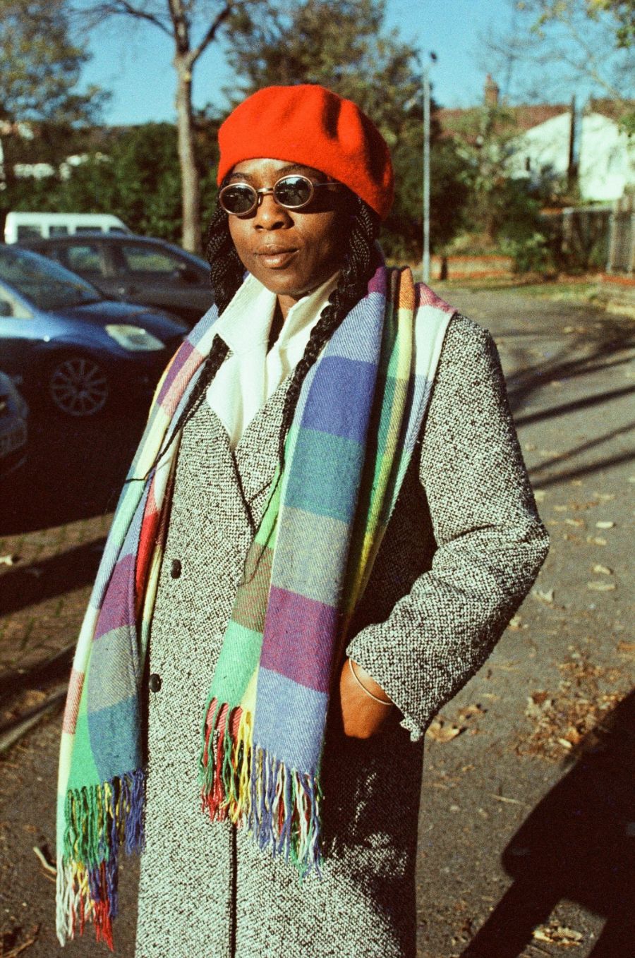 Woman wearing a red beanie, sunglasses, and a colorful scarf outdoors.