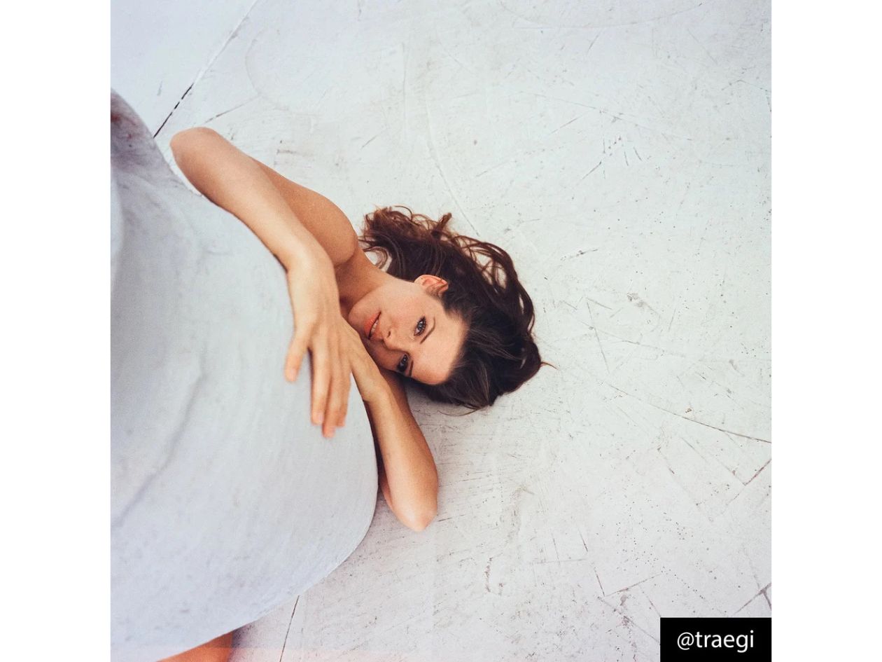 Woman lying on a textured white floor wearing a light dress.