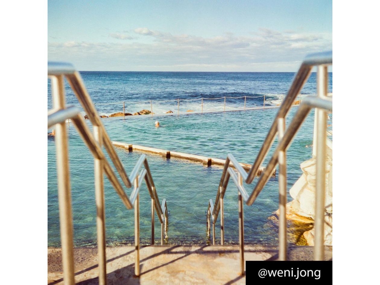 Metal staircase leading down to a pool with ocean view, clear blue water, and sky.