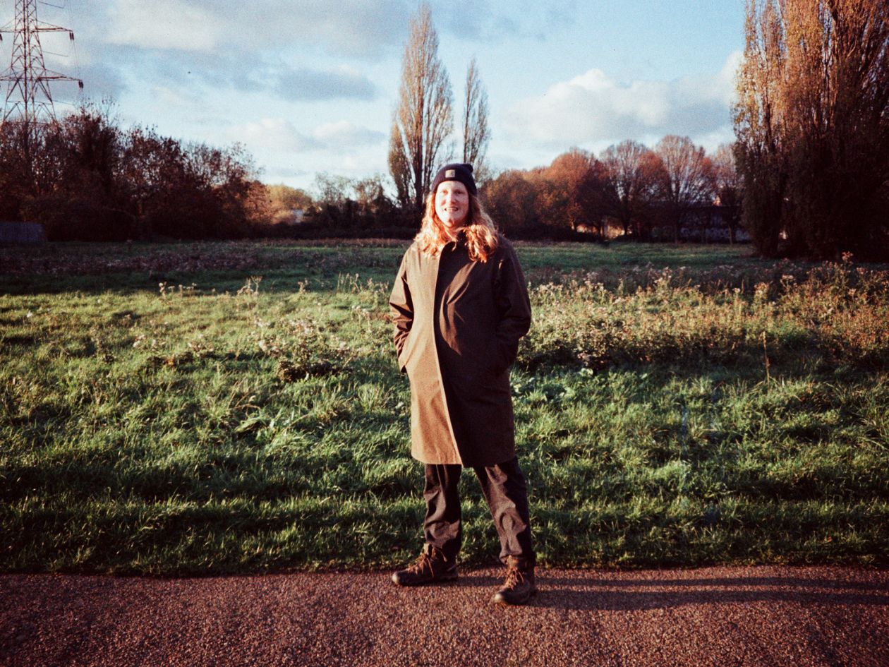 Person standing in a field with trees and power lines in the background.