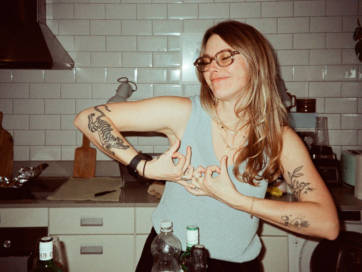 Woman with tattoos and glasses in a kitchen.