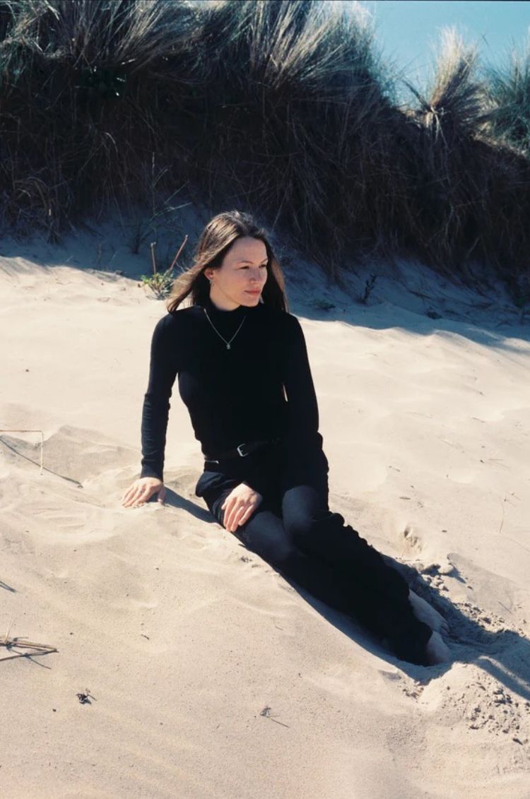 Person sitting on sand dunes with tall grasses in the background
