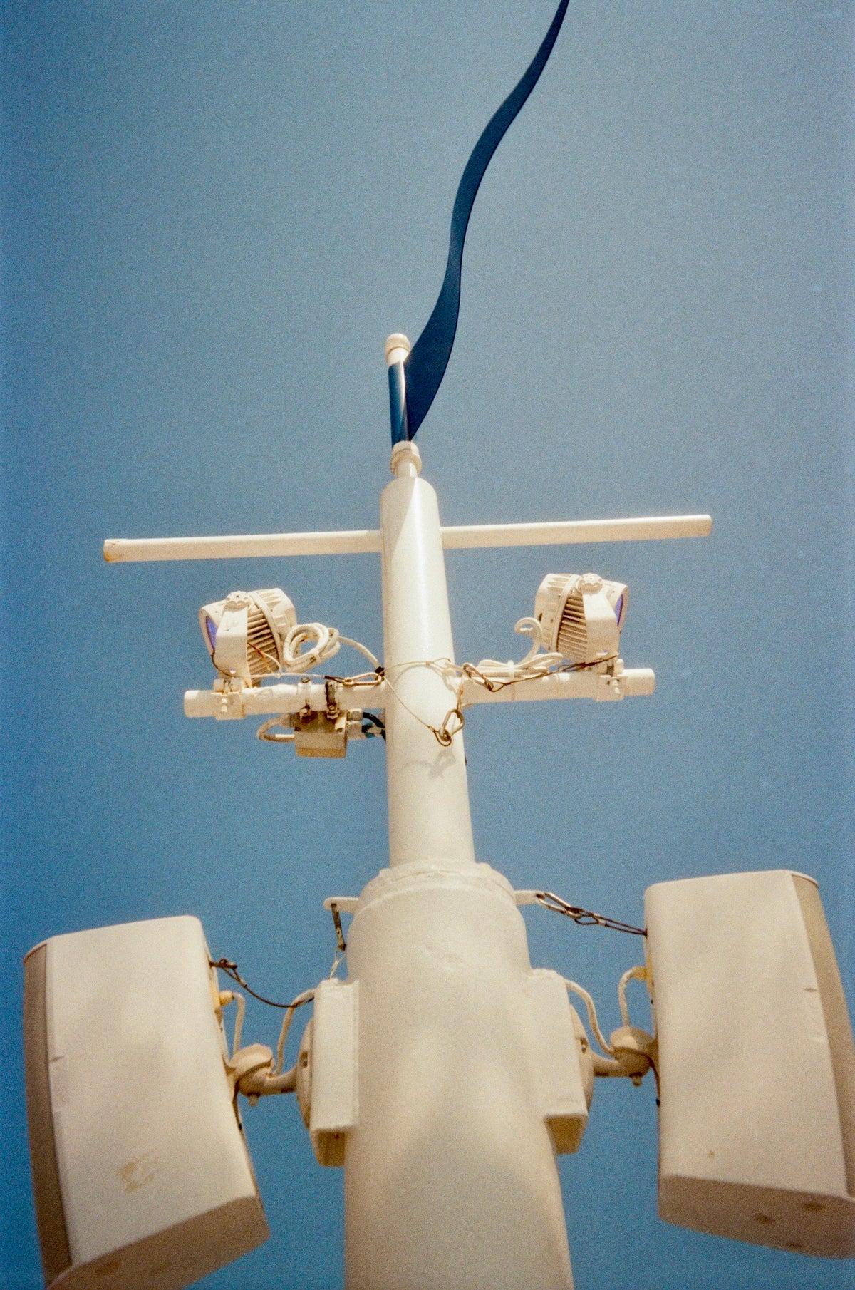 Sample photo for the Kodak EC35 film camera. A close-up low-angle view of a white mast or antenna structure with attached speakers and a dark blue ribbon or flag at the top, set against a clear blue sky.