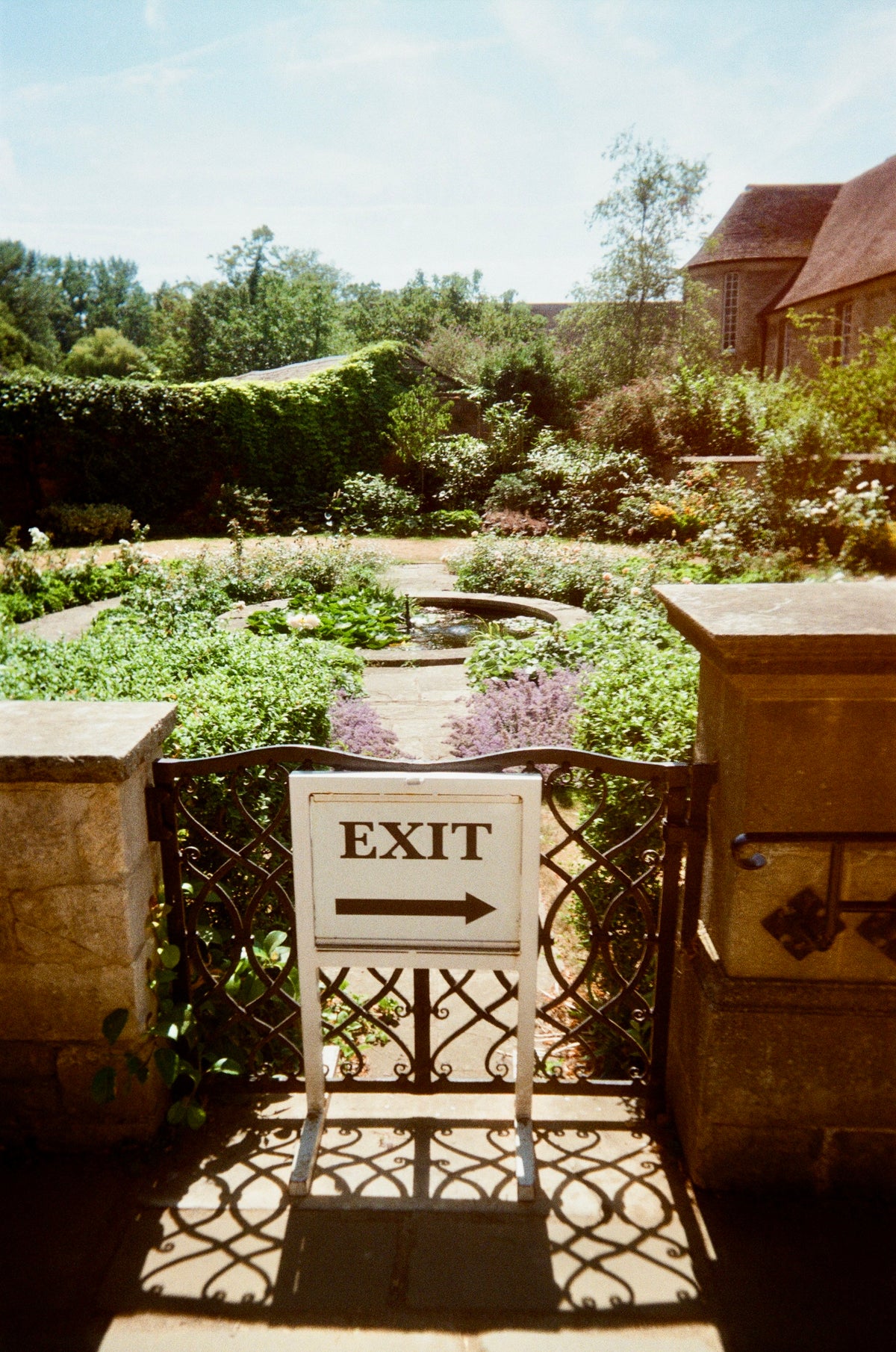 Sample photo for the Kodak EC35 film camera. A white sign with the word 'EXIT' and a black arrow pointing right, mounted on a wrought-iron gate in a garden setting with stone pillars and greenery in the background.