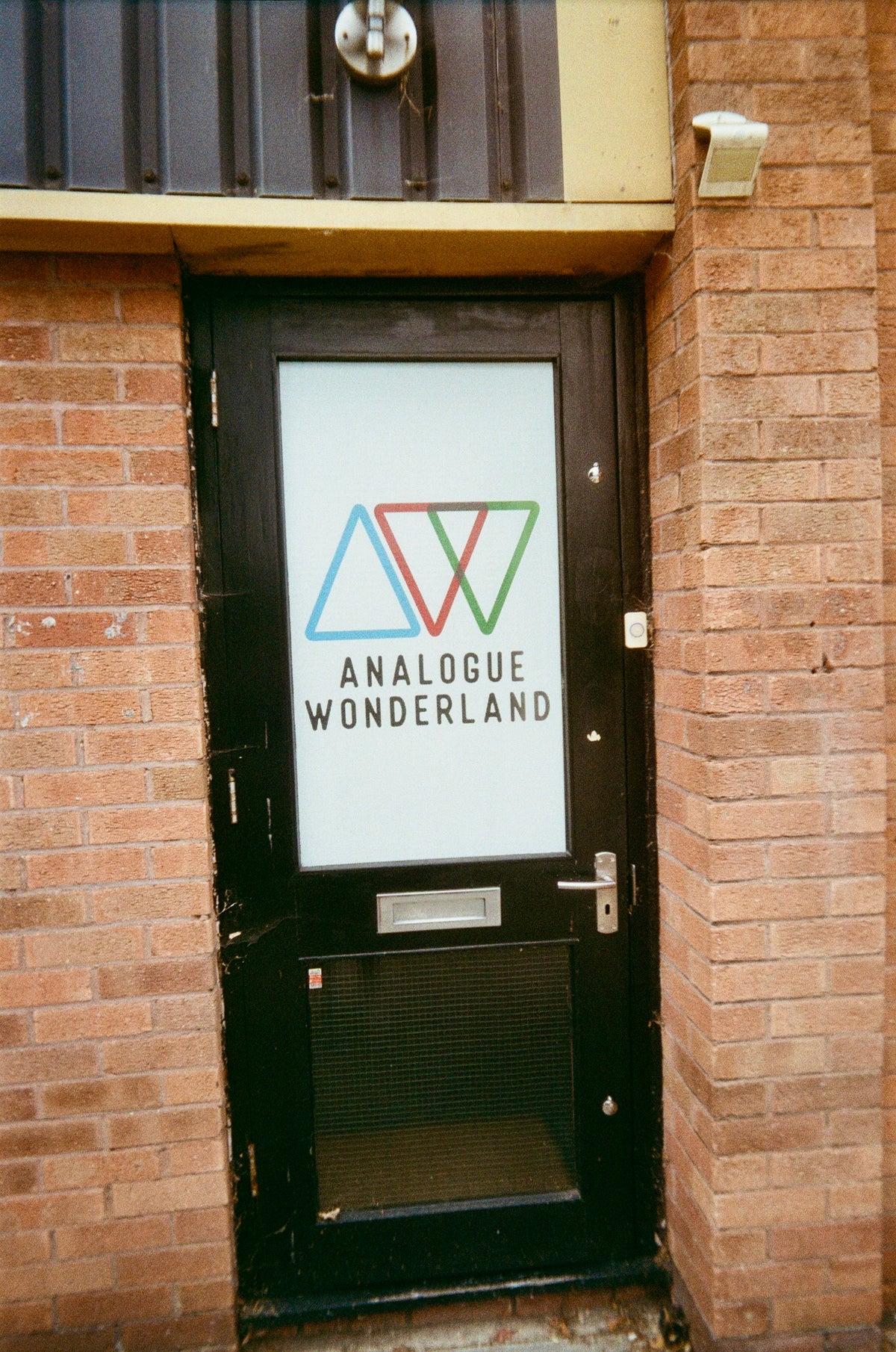 Sample photo for the Kodak EC35 film camera. A black metal door with a large white sign reading 'ANALOGUE WONDERLAND' and a colorful triangle logo, set in a brick building.