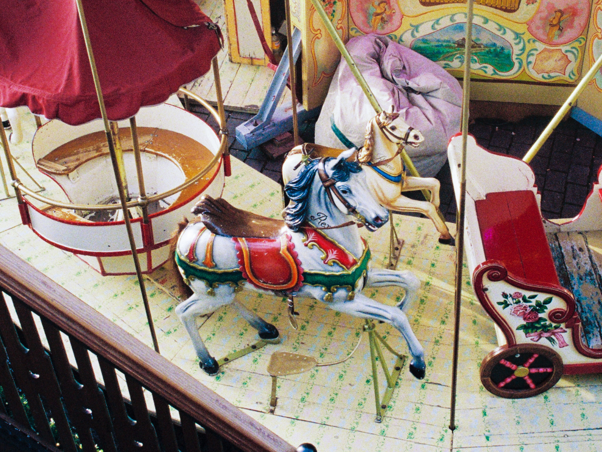 Colorful carousel horse on a wooden floor with other carousel elements in the background.