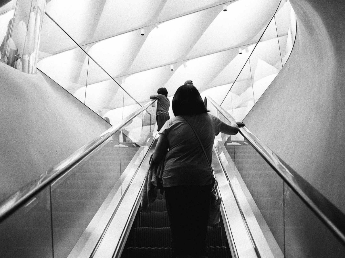 Two people ascending an escalator in a modern architectural setting.