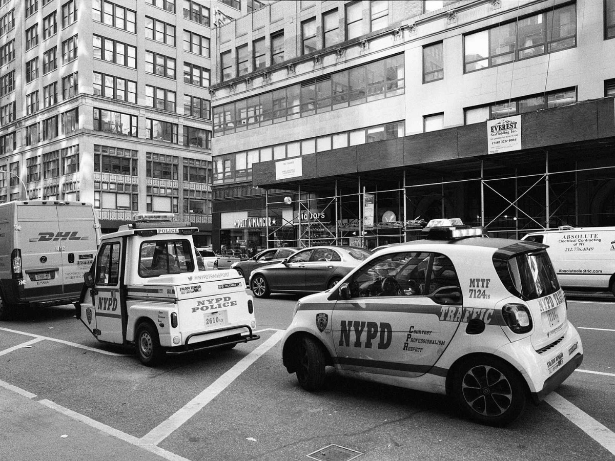 Two NYPD vehicles on a city street with tall buildings in the background.