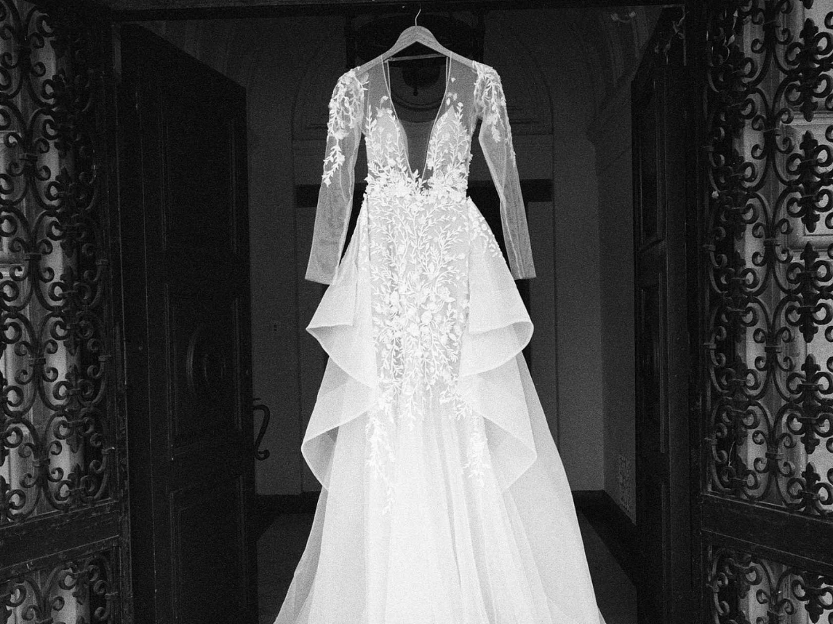 White wedding dress with intricate detailing hanging against a dark, ornate background