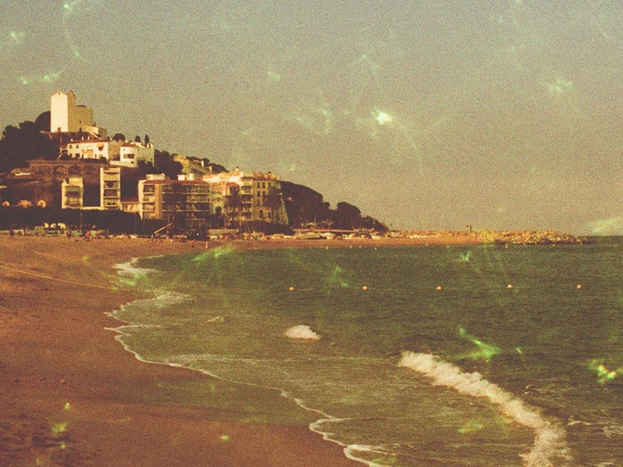 Coastal scene with buildings on a hill overlooking a beach and ocean with subtle gemstone green effects across the frame.
