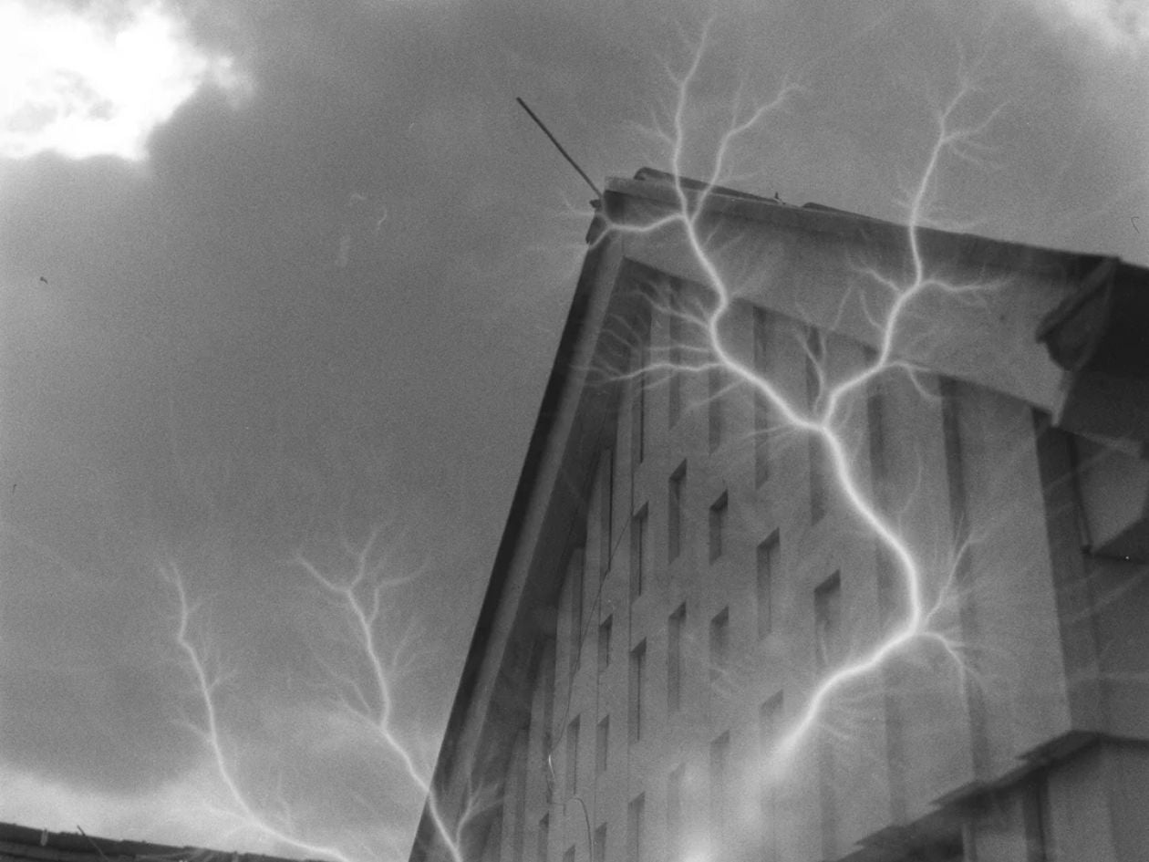 A building roof reaching into a cloudy sky, with lightning-like patterns branching across the frame.