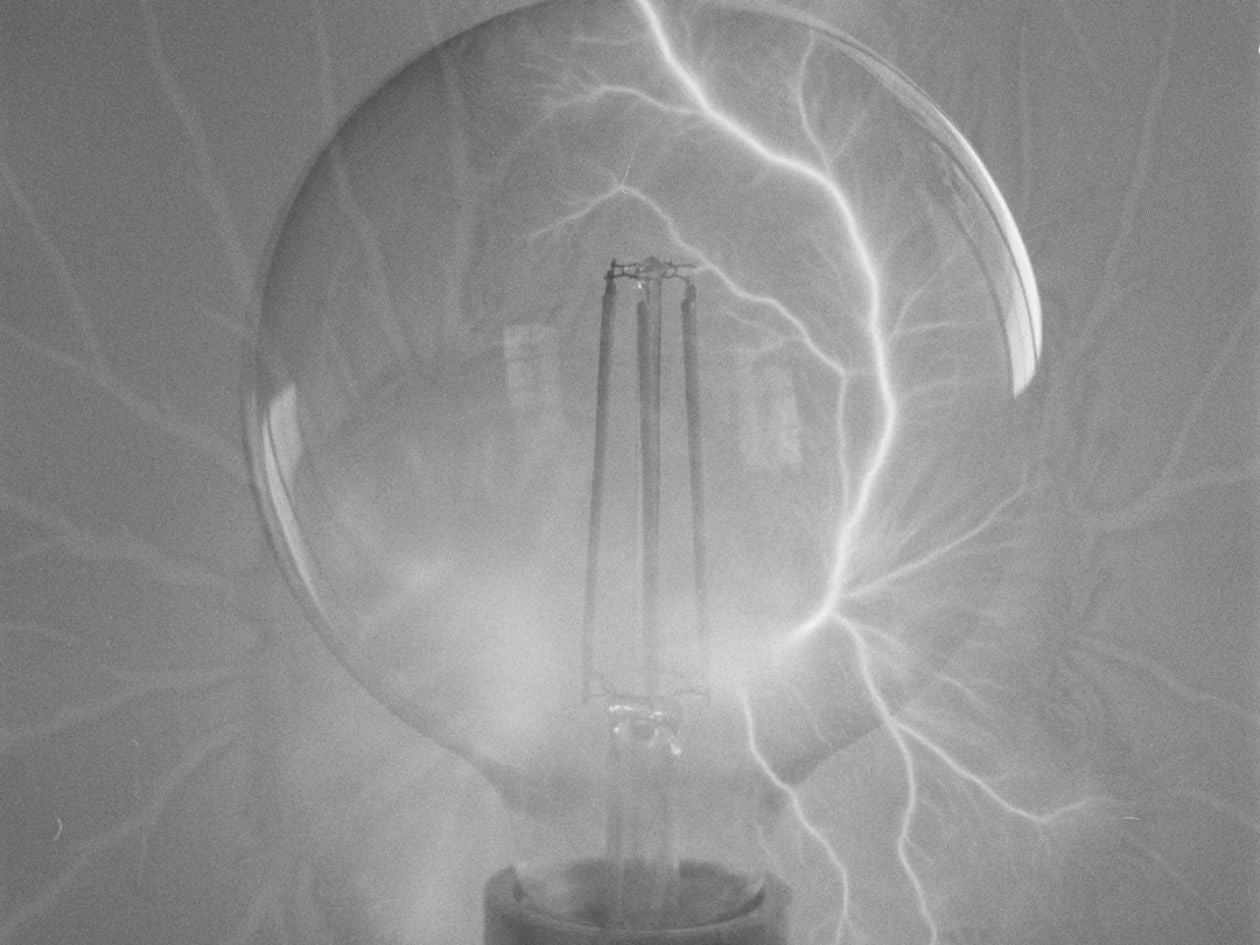 A close-up of a light bulb with white lightning-like patterns radiating across the frame.